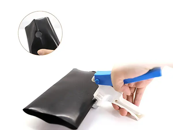 A hand is holding a drip tape hole punch to punch a pipe.